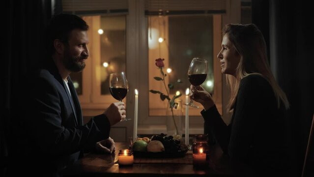 Date, Valentines Day, cheers. Man and woman have dinner by candlelight at home or in restaurant, taste wine and cheers
