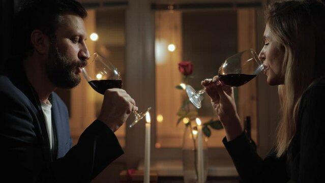 Date, Valentines Day, cheers. Man and woman talk and drink red wine in romantic setting by candlelight