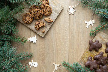 Christmas gingerbread man and chocolate chip cookies. Holiday season winter flat lay composition with fir tree branches and copy space on wooden background.