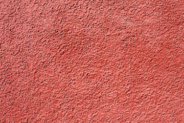 Home facade texture. Red rough surface. Grunge grain. Crushed rocks in the wall. Exterior home decoration. Stucco wall pattern. Red color retro design. Noisy design background.