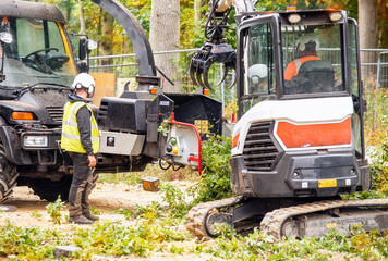 Arborist using a wood chipper machine for shredding trees and branches. The tree surgeon is wearing...