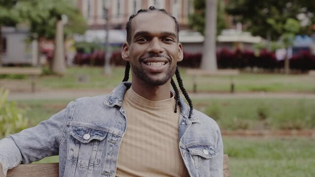 Jovem negro, sentado no banco da praca, sorrindo. Cinematico 4k.
