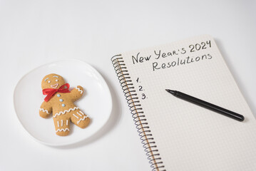 Phrase New Year's Resolutions 2024 in the notebook and pen. Gingerbread man on table