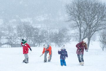 Big family with children play snowballs outside during snowfall. Winter fun holidays. Games in...