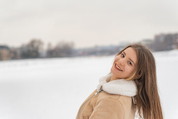 Smiling girl in trendy beige sheepskin coat have fun in snowy clearing. Woman rejoices in frosty winter day