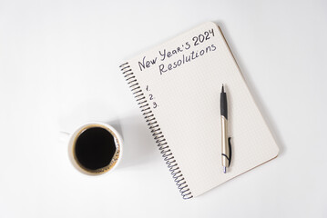 Phrase New Year's Resolutions 2024 in the notebook and pen. Cup of coffee on table - obrazy, fototapety, plakaty