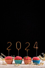 Holiday cupcake with pink glaze and 2024 numbers on black background. New Year and Christmas....