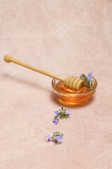 Fototapeta premium natural honey in a glass bowl with a wooden spoon and fresh rosemary sprigs in bloom