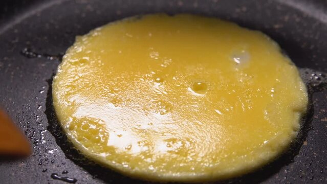 Close-up round egg yolk pancake is flipped over with a spatula