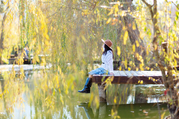 Autumn lake woman. She sits by a pond on a wooden pier in autumn and admires nature. The concept of...