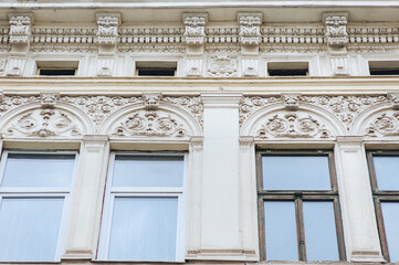 Four large old windows with wooden frames and ornamental reliefs on the wall. Neoclassical building, facade of an old house in Lviv, Ukraine.