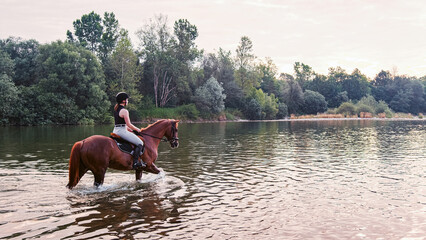 Rider girl crossing the calm river water riding their beautiful horses on the cloudy summer day....