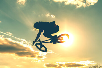 Man on bmx bike against sunshine sky. High BMX jump. Biker silhouette doing an jump.