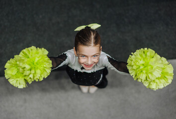 Smiling girl athlete cheerleader in a suit with pompoms, an 8-year-old child with makeup, face...