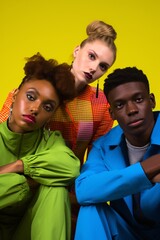Obraz premium four young people sitting together on a yellow background, bold fashion, colorful costumes, queer academia
