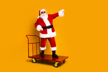 Fototapeta na wymiar Full size portrait of charismatic aged santa stand store trolley showing empty space new year ad isolated on yellow color background