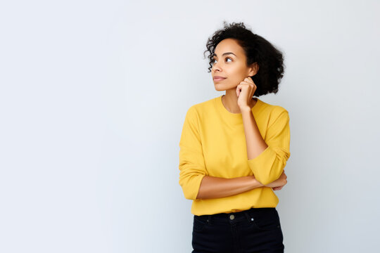 Jeune femme en train de penser en regardant sur le c&ocirc;t&eacute; vers le haut, espace libre pour du texte ou mise en sc&egrave;ne, tenue jaune fond uni gris p&acirc;le