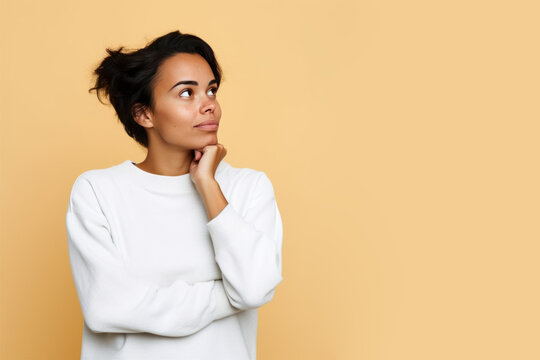 Jeune femme en train de penser en regardant sur le c&ocirc;t&eacute; vers le haut, espace libre pour du texte ou mise en sc&egrave;ne, tenue blanche fond uni beige p&acirc;le