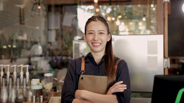Cheerful barista woman running coffee shop business entrepreneurship standing in front of counter bar in cafeteria Asian female small business start-up smiling arm crossed looking at camera confident