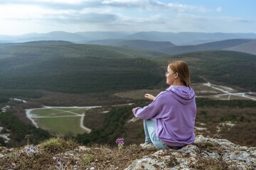 Girl on mountain peak looking at beautiful mountain valley in fog at sunset in summer. Landscape with sporty young woman, foggy hills, forest, sky. Travel and tourism, hiking
