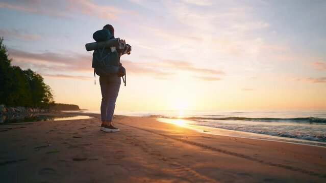 Woman tourist takes photo of sea sunset. Female hiker camper with touristic backpack recording video of nature on smartphone enjoying vacations. Travel tourism trip hiking camping wanderlust concept.