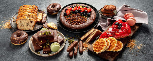 Tasty cake, cookies, waffles, macaroons, muffin. Delicious desserts on dark background. Food concept