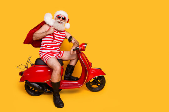 Full length photo of funny positive elderly guy wear new year swimsuit hat delivering presents empty space isolated yellow color background