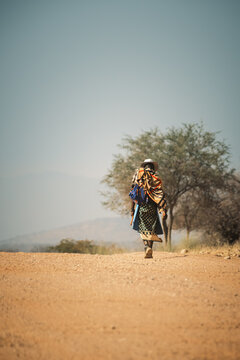 Local man in traditional attire walking on roadside of highway C43 near Epupa Falls, Kunene Region, Namibia.