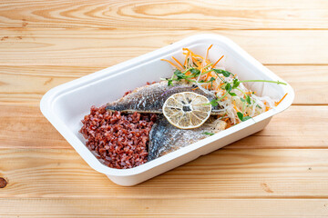 Baked sea bass with red rice. Healthy diet. Takeaway food. Eco packaging. On a wooden background.