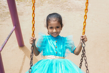 Happy little indian girl having fun on a swing on sunny day. Healthy summer activity for children.