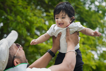 Beautiful Young indian father throwing baby boy up in air and catching, amusing kid and having fun together in the park.