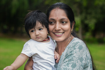 Happy young indian mother with her cute looking boy smiling, playing and enjoying in public park or garden.