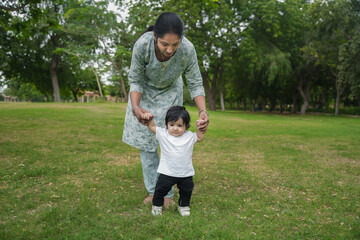 Young indian mother with her cute looking boy walking in garden, Teaching her boy to walk.