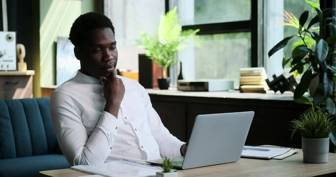 A black man experiences a eureka moment during his work with laptop. The spark of a brilliant idea illuminates his face as he continues his creative process.