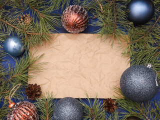 Crumpled sheet of craft paper with copy space for Christmas text, blue ball, glittering brown baubles, natural fir branches, New Year festive decoration. Xmas creative greeting template