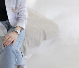 light leather bracelet on a light background. hommade bracelet on the girl's arm. A girl seated on a bed in a room is wearing a lovely bracelet on her wrist, dressed in light jeans.
