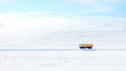 Distant view of a yellow truck advancing on a snowy rural road. Minimal tranquil scene depicting the concept of reaching a destination.