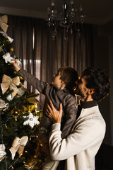 Happy family father, mother and son decorate the New Year tree, have fun, dance and unpack gifts. Christmas and New Years Eve concept. Vertical shot