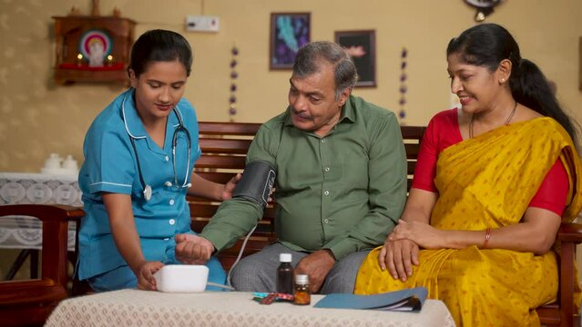 Nurse checking blood pressure of elderly man while with caring wife at home - concept of medical or healthcare assistance, consultation and professional occupation