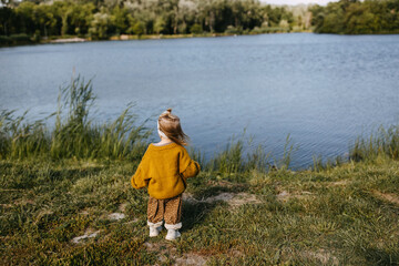 Naklejka na ściany i meble Child alone standing by the lake on a sunny day, watching it.