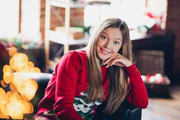 Photo of cute adorable schoolgirl with blond hairstyle wear red sweater sit on armchair hand on cheek staring at new year at home indoors