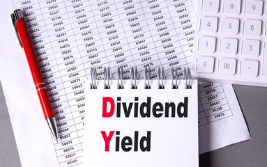 DIVIDEND YIELD text on notebook with pen, calculator and chart on grey background