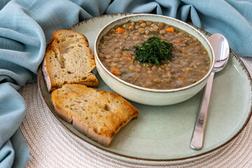 Homemade green lentils soup with bay leaves and dill in a green ceramic pot, with toast. Vegetarian Mediterranean dish. Close up