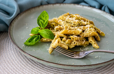 Penne with pesto sauce, sour cream and basil, on a green ceramic plate. Mediterranean dish, closeup. Home cooking, healthy eating.