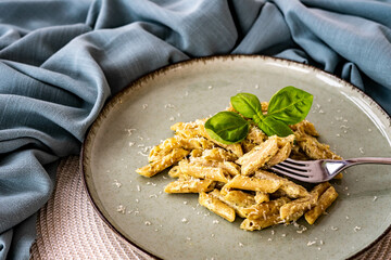 Penne with pesto sauce, sour cream and basil, on a green ceramic plate. Mediterranean dish, closeup. Home cooking, healthy eating.