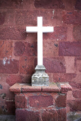 A white Christian cross against a deep red brick wall of a church. 
