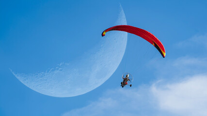 Man doing paramotor flying in front of the moon.