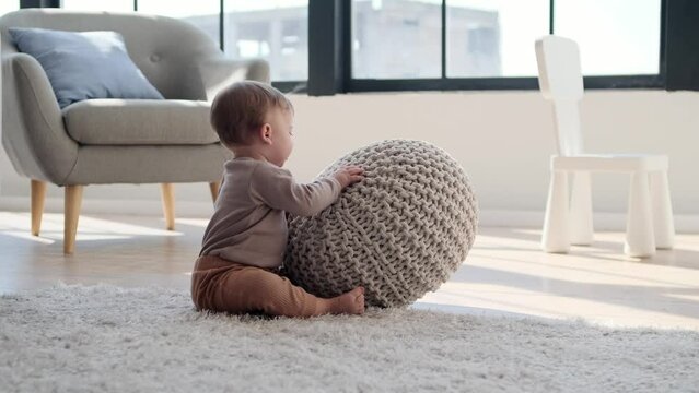 Bright-eyed little boy finds endless delight in playing with a pouf. His infectious laughter fills the room as he explores, bounces, and creates imaginative games with cushiony companion.