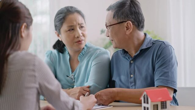 Asian mature couple thinking about buying real estate.Happy senior old aged woman and man customer landlord hold key to new house apartment,signing contract deal of loan pension mortgage at home.