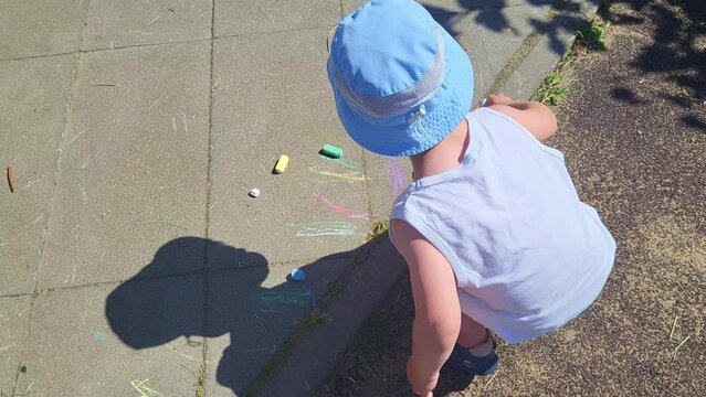 Baby is sitting and drawing with crayons on a tile near the playground. Baby aged two years (two-year-old boy)